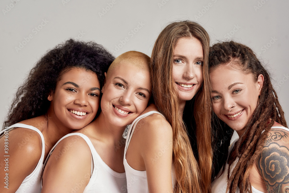 Close up portrait of four cheerful young diverse women, female friends smiling at camera while posing together isolated over grey background Close up portrait of four cheerful young diverse women, female friends smiling at camera while posing together isolated over grey background
