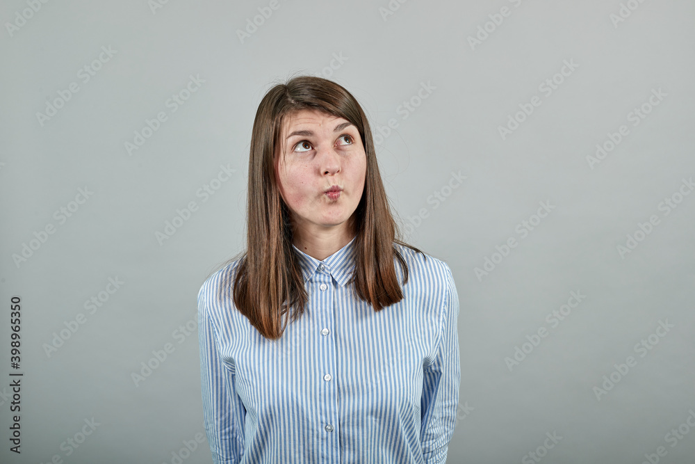 thinking about question, pensive expression. Doubt. Thoughtful face. Using that incredibly sharp business mind. Young attractive woman, dressed blue shirt brown eyes, brunette hair, grey background thinking about question, pensive expression. Doubt. Thoughtful face. Using that incredibly sharp business mind. Young attractive woman, dressed blue shirt brown eyes, brunette hair, grey background