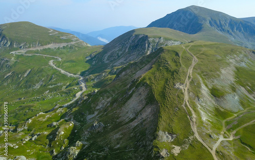 Aerial drone panorama of Transalpina road winding along sharp mountain peaks. The alpine grasslands of Parang Mountains are rocky and green. Carpathia, Romania