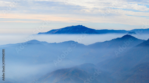 Buila Massif crests seen from Cozia Mountain peak. The mountain sides are rising from a dense layer of clouds. Fog is surrounding the high peaks. Carpathia, Romania