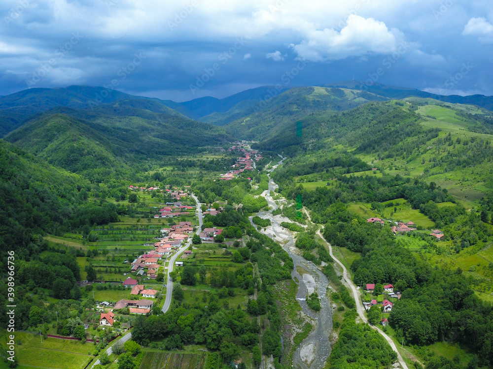 Aerial drone view of Novaci village and Gilort river Valley in a stormy, cloudy day. The Parang Mountains Massif can be seen in the background covered by dark clouds. 