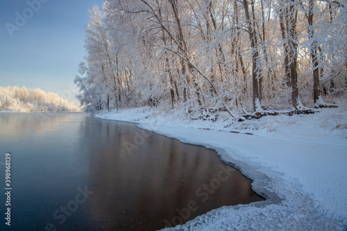 Winter day on the river  partially covered with ice. On the shore there are trees in hoarfrost.