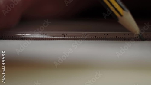 A slate pencil draws a line along a ruler on a white piece of paper. Drawing or sketching.