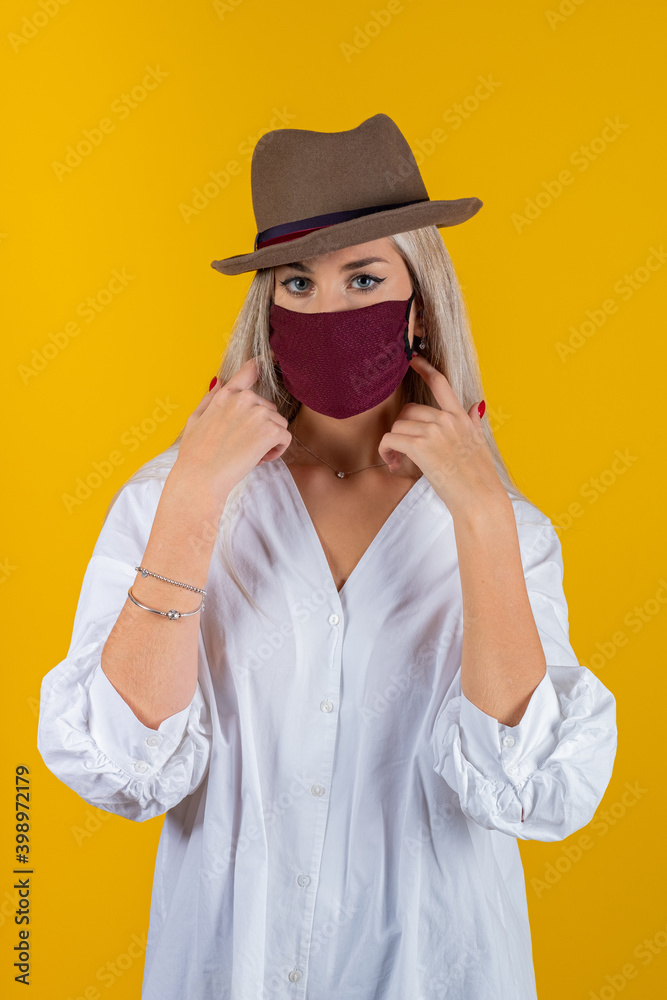 Woman wearing stylish protective face mask and brown cap, posing on yellow background. Trendy Fashion accessory during quarantine of coronavirus pandemic. Close up studio portrait Woman wearing stylish protective face mask and brown cap, posing on yellow background. Trendy Fashion accessory during quarantine of coronavirus pandemic. Close up studio portrait