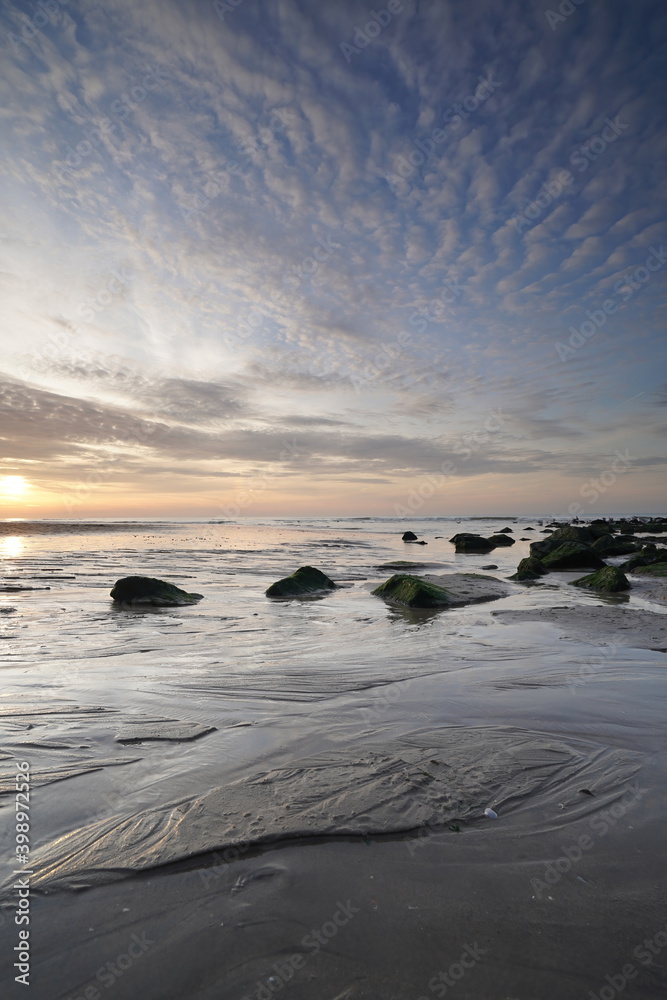 Sunset on the beach. Seascape with an impressive blue, orange sky. Green rocks in foreground