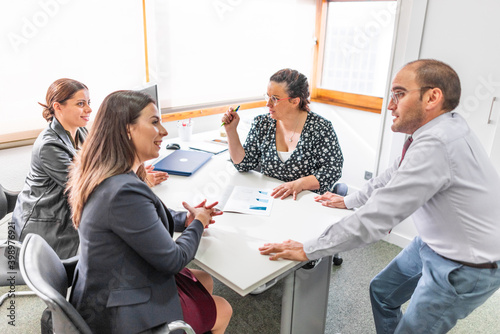 business meeting 4 people with laptops ipad tablet folios pens and folios in bright office with large windows three women and a man happy smiling