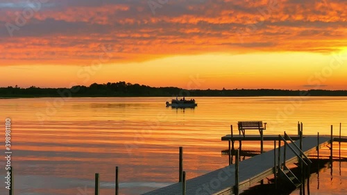 Beautiful Lake Irving in Bemidji Minnesota, the first lake on the Mississippi River, is seen at sunset as a pontoon with fishermen floats past a boat dock on a calm evening.