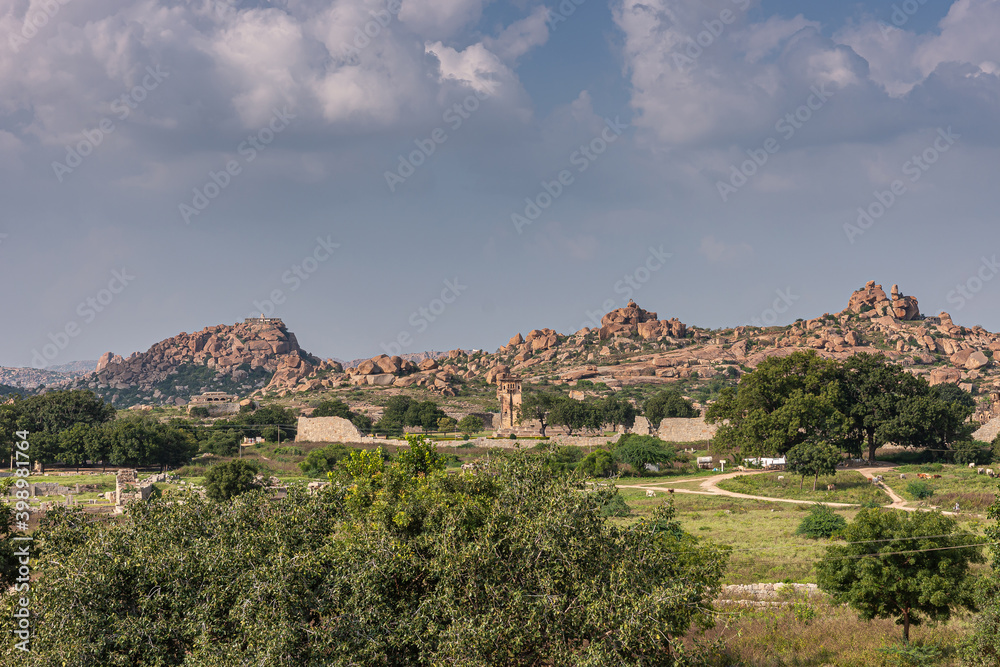 Hampi, Karnataka, India - November 4, 2013: Royal Enclosure. Wide shot of the scenery around and above with the Mohammadan Watch Tower about in center. Rocky hills under blue sky. Green vegetation.