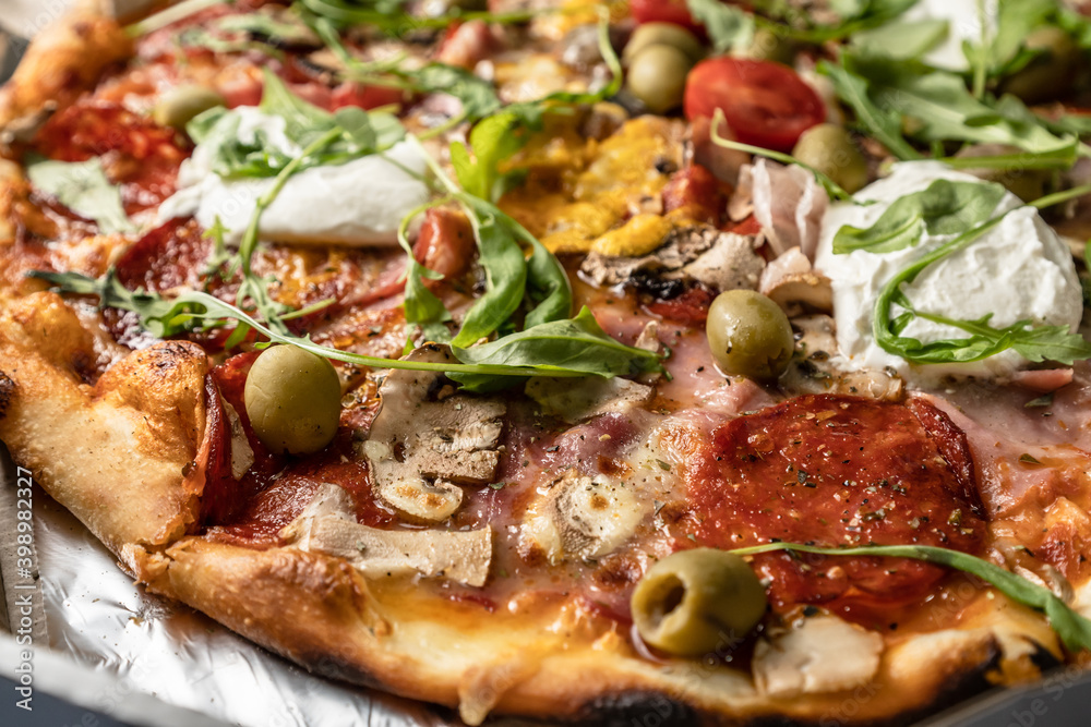 Baked pizza with salami, prosciutto, olives and arugula with red sauce and melted cheese on the table, close up Baked pizza with salami, prosciutto, olives and arugula with red sauce and melted cheese on the table, close up