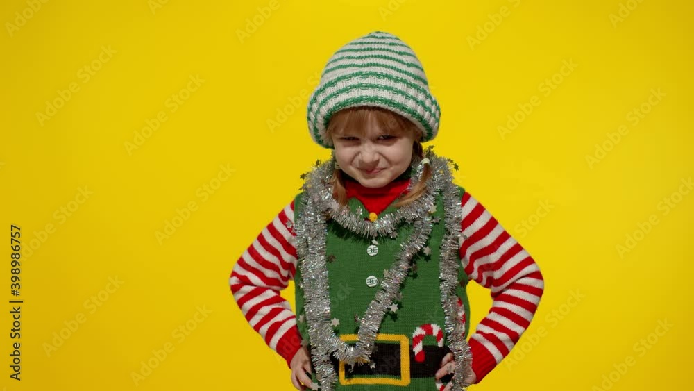 Displeased little blonde kid teen teenager girl in Christmas elf Santa helper costume isolated on yellow studio background. Child looking unhappily angry, sad at camera. Negative emotions and reaction Displeased little blonde kid teen teenager girl in Christmas elf Santa helper costume isolated on yellow studio background. Child looking unhappily angry, sad at camera. Negative emotions and reaction