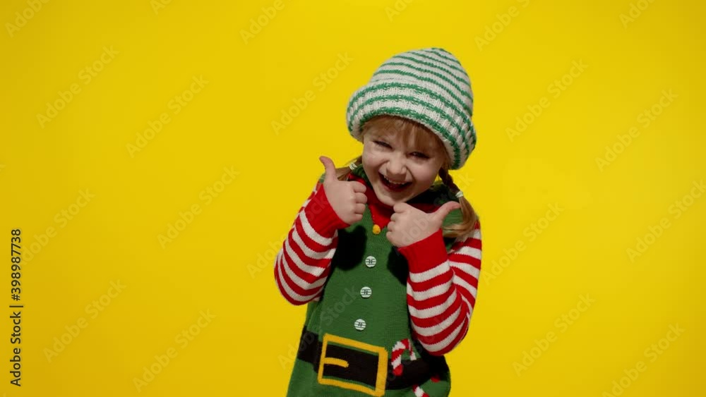 Teen small kid girl 5-6 years old in Christmas elf Santa helper costume laughing, showing thumbs up gesture isolated on yellow background. Child fooling around. People New Year holidays. 6k downscale Teen small kid girl 5-6 years old in Christmas elf Santa helper costume laughing, showing thumbs up gesture isolated on yellow background. Child fooling around. People New Year holidays. 6k downscale