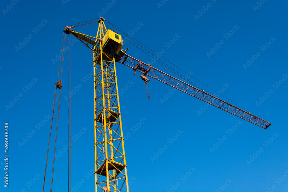 a yellow tower crane in operation against blue sky