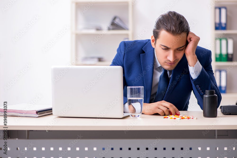 Young male employee and a lot of pills on the desk Young male employee and a lot of pills on the desk