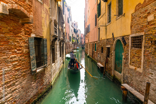 Venetian gondolier punting gondola through green canal waters of Venice Italy © Pawel Pajor
