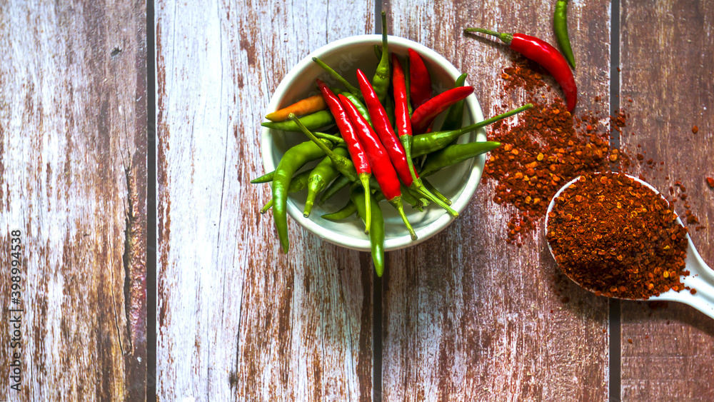 Hot red chili in a white bowl and chili flakes in a white spoon on a dark wood floor. Hot red chili in a white bowl and chili flakes in a white spoon on a dark wood floor.