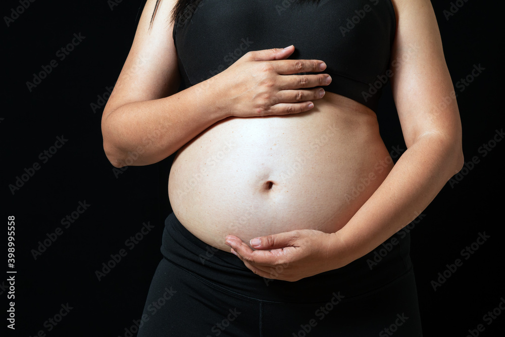 Asian woman feeling worry and placing hand on stomach on black background. Concept of weight loss for good health with excercise. Asian woman feeling worry and placing hand on stomach on black background. Concept of weight loss for good health with excercise.