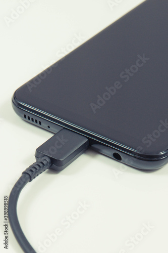 Plug of charger connected to black mobile phone. Smartphone charging