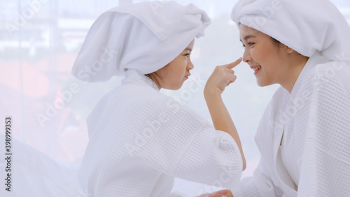 Mother with little daughter in bathrobes doing beauty treatment together in bedroom.