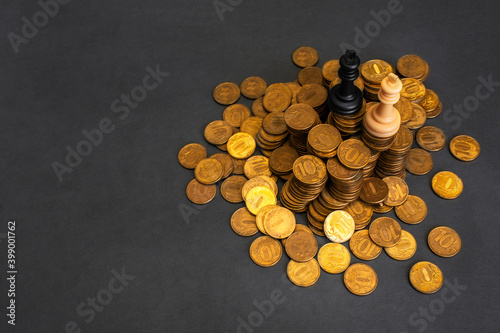 Government corruption concept. Black and white chess kings on top of huge pile of gold shiny coins against grey grunge background with space for text. Copy space. Top view