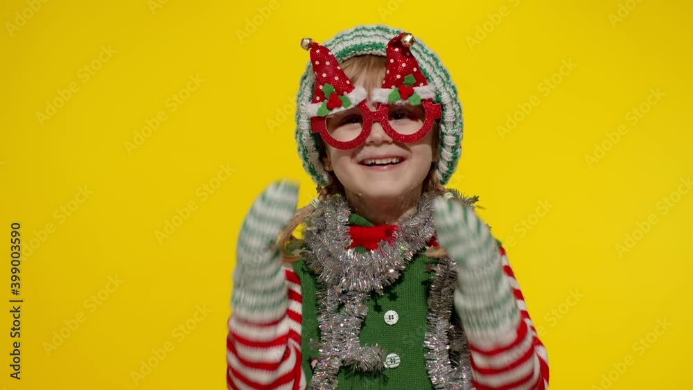 Happy fun blonde kid teen girl in Christmas elf Santa helper costume with funny glasses posing isolated on yellow background. Joyful child dancing, fooling around. People New Year holidays celebration Happy fun blonde kid teen girl in Christmas elf Santa helper costume with funny glasses posing isolated on yellow background. Joyful child dancing, fooling around. People New Year holidays celebration