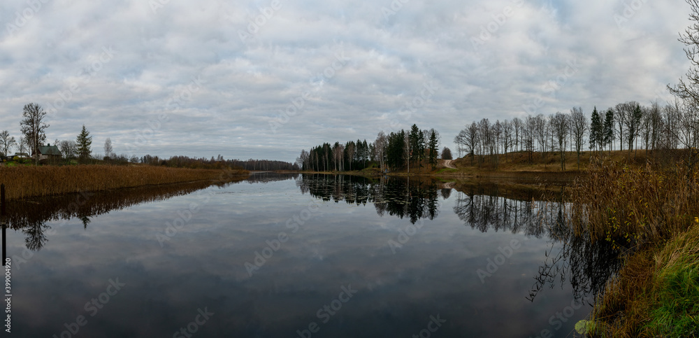 Opposite bank of lake in the autumn, cloudy sky, late autumn, bare tree silhouettes and reflections in the water