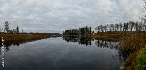 Opposite bank of lake in the autumn, cloudy sky, late autumn, bare tree silhouettes and reflections in the water