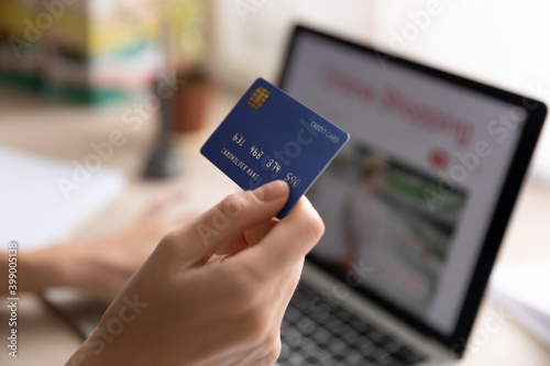 Close up woman holding plastic credit card, using laptop, paying online, young female entering information, browsing banking service, checking balance, shopping in internet, ordering goods