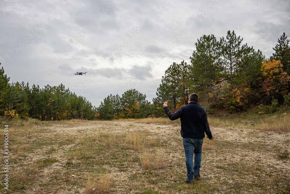 A man walks with his drone in a pine forest on a cloudy autumn day