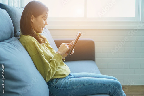 Young woman using tablet sit on sofa at home, user holding tablet looking at screen reading e-book app online relax on leisure with device work study online on couch