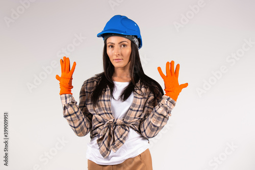 Young handywoman in hard hat and protective gloves posing on white background. Construction and gender stereotypes. photo