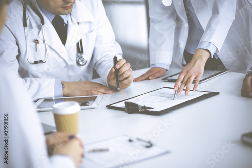 Group of unknown doctors are sitting at the desk and discussing medical treatment, using a clipboard, close-up. Team of physicians at work in a clinic. Medicine and healthcare concept