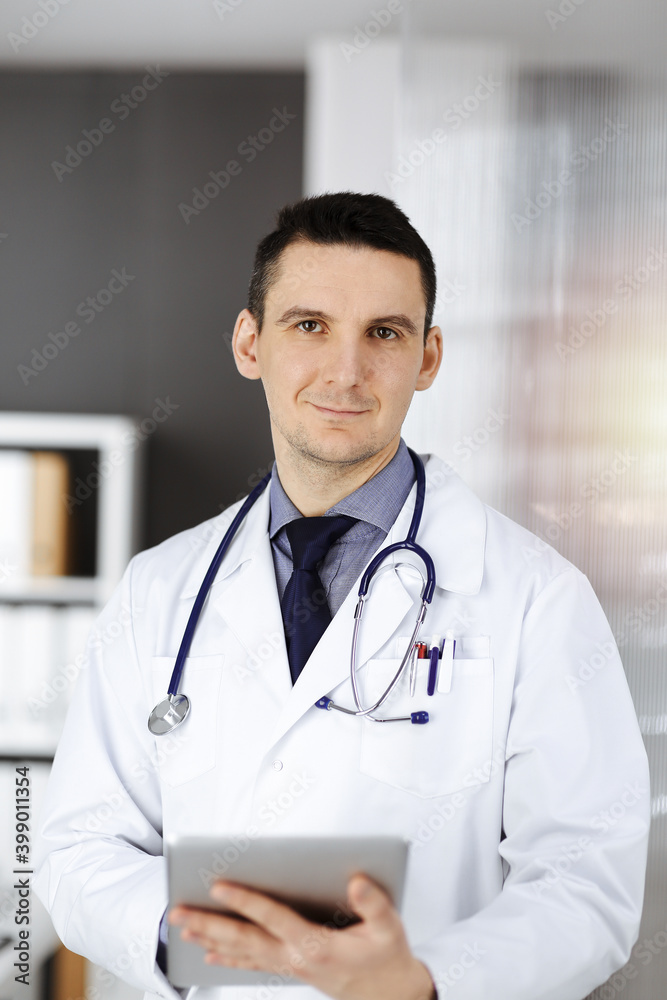Friendly male doctor using tablet computer in sunny clinic. Medicine and healthcare concept Friendly male doctor using tablet computer in sunny clinic. Medicine and healthcare concept