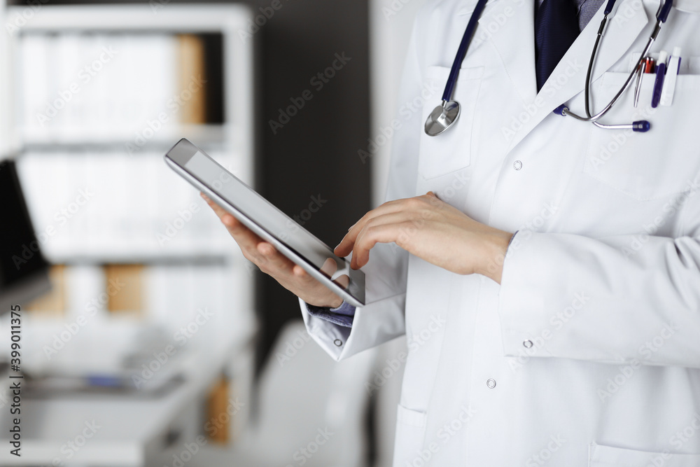 Unknown male doctor using tablet computer in clinic near his working place, closeup. Perfect medical service in hospital. Medicine and healthcare concept Unknown male doctor using tablet computer in clinic near his working place, closeup. Perfect medical service in hospital. Medicine and healthcare concept