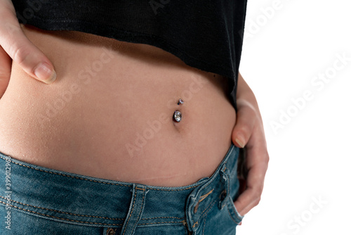Belly button or navel piercing, of young woman wearing jeans isolated on white.