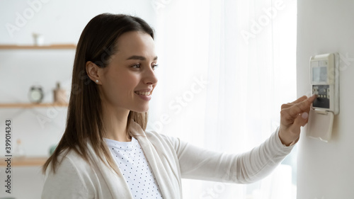 Smiling young woman pressing buttons on smart house system close up, standing at home, happy girl customer using air conditioning controller on wall, setting alarm password or comfort temperature