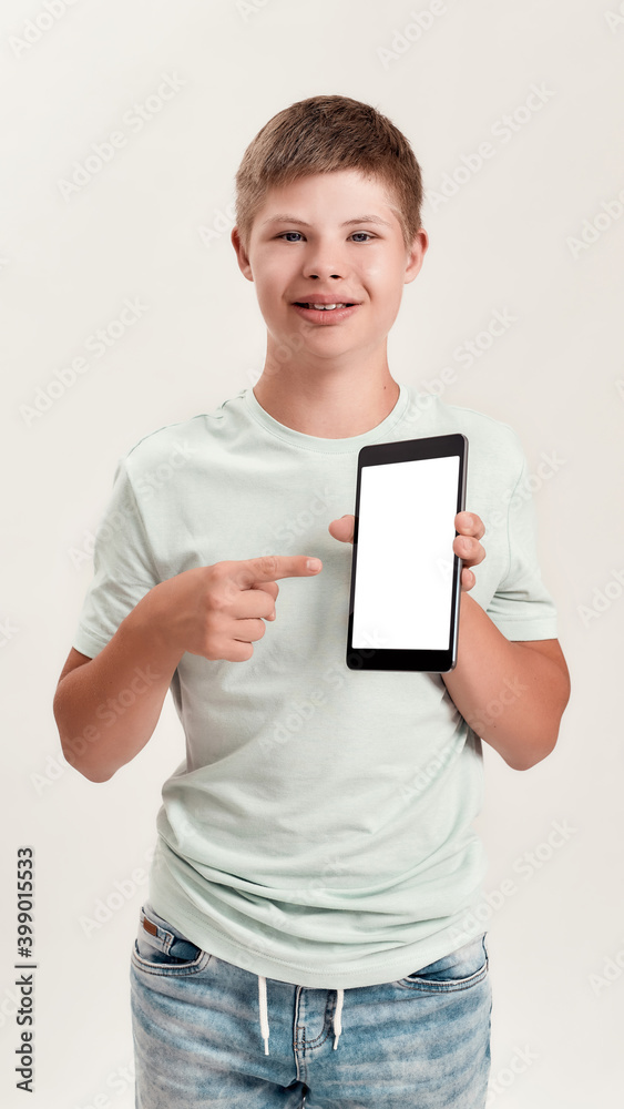 Happy disabled boy with Down syndrome smiling, holding and pointing at tablet pc with blank screen while standing isolated over white background