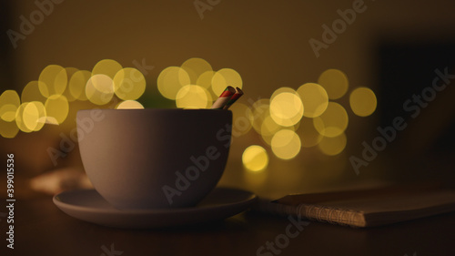 blue cup with hot cholate on table with christmas lights on background in dark evening light