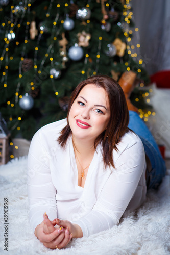 Fotografie A beautiful plus size brunette in a white blouse and jeans lies on the floor aga