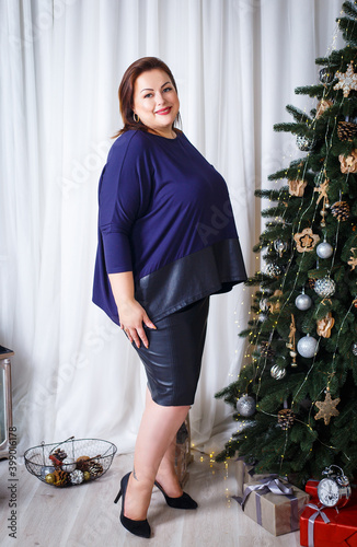 Obraz na plátně Beautiful plus size girl in a blue blouse with a leather insert near a christmas