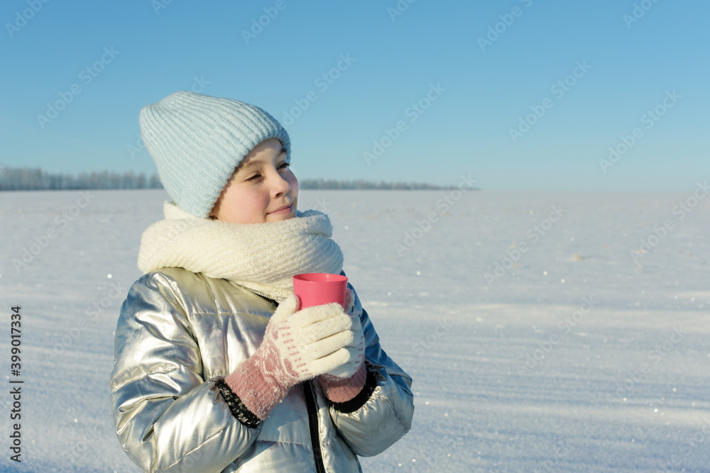 Cute teen girl in winter clothes with cup of hot drink in nature in frosty sunny day