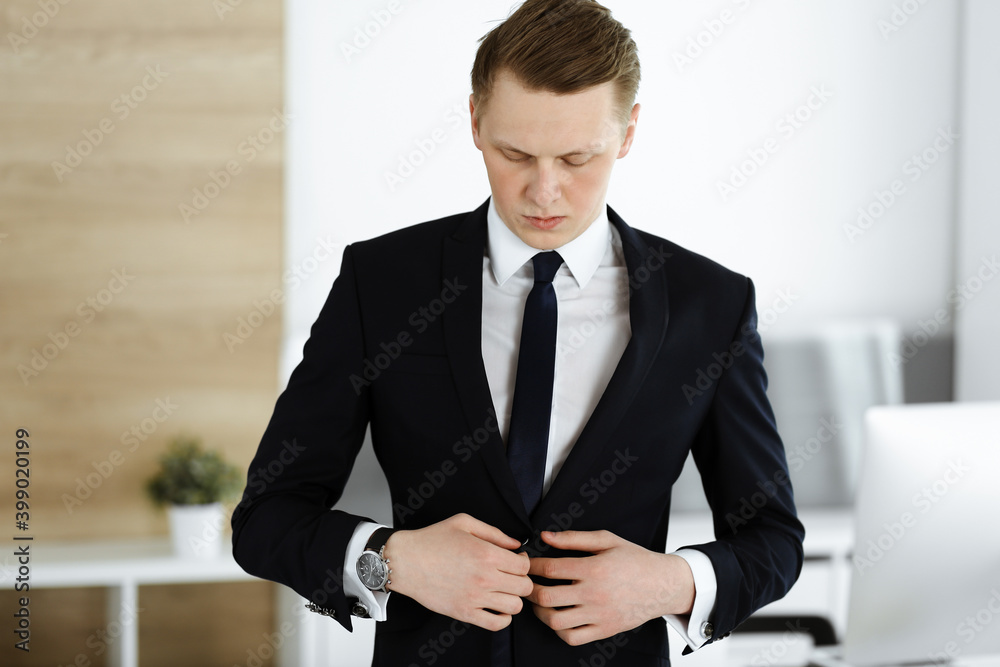 Cheerful businessman standing and looking at camera in office. Headshot of young and successful entrepreneur Cheerful businessman standing and looking at camera in office. Headshot of young and successful entrepreneur