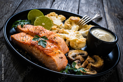Roasted salmon steaks with fried cauliflower, fried brown champignons, lime and mayonnaise on wooden table 
