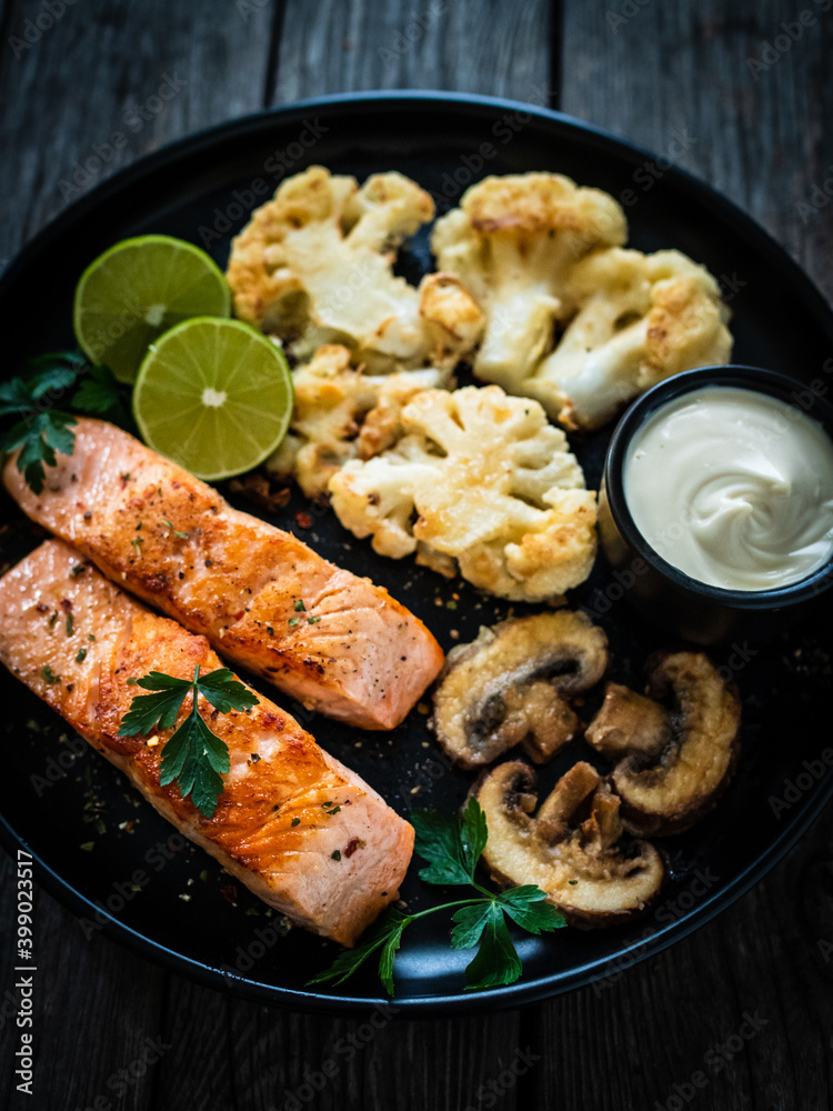 Roasted salmon steaks with fried cauliflower, fried brown champignons, lime and mayonnaise on wooden table
Roasted salmon steaks with fried cauliflower, fried brown champignons, lime and mayonnaise on wooden table