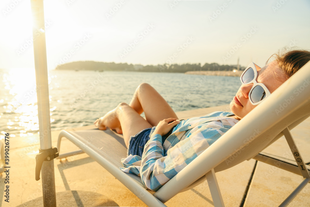 young woman resting at sun lounger at sunset