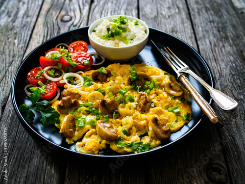 Delicious breakfast - scrambled eggs with fried champignon, cottage cheese and vegetable served on black plate on wooden table