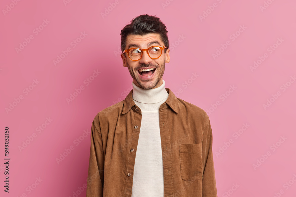 Φωτογραφία Studio shot of handsome adult European man with glad expression has fun and looks aside wears turtleneck brown shirt isolated over pink background