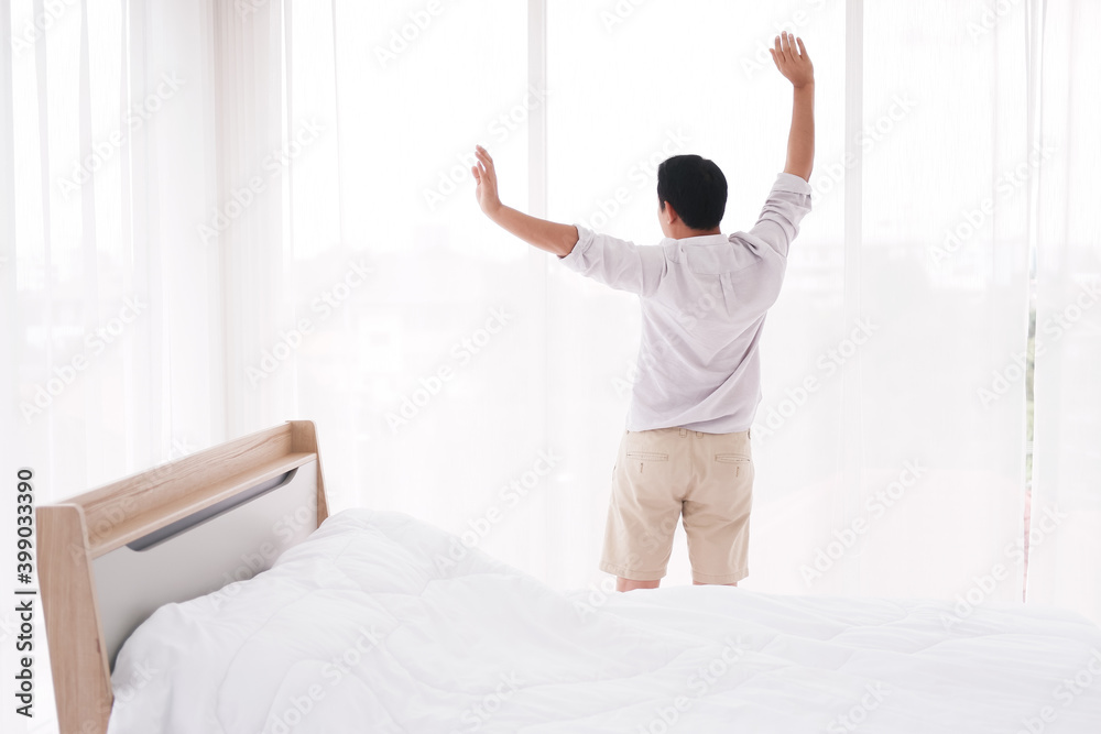 Asian man is Stretching lazily after waking up in bedroom. He felt refreshed after taking a nap. Asian man is Stretching lazily after waking up in bedroom. He felt refreshed after taking a nap.