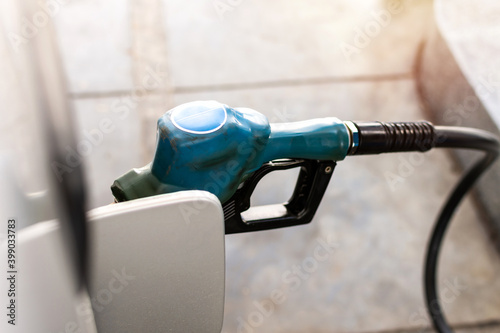 White car refueling at gas station with blue fuel nozzle.