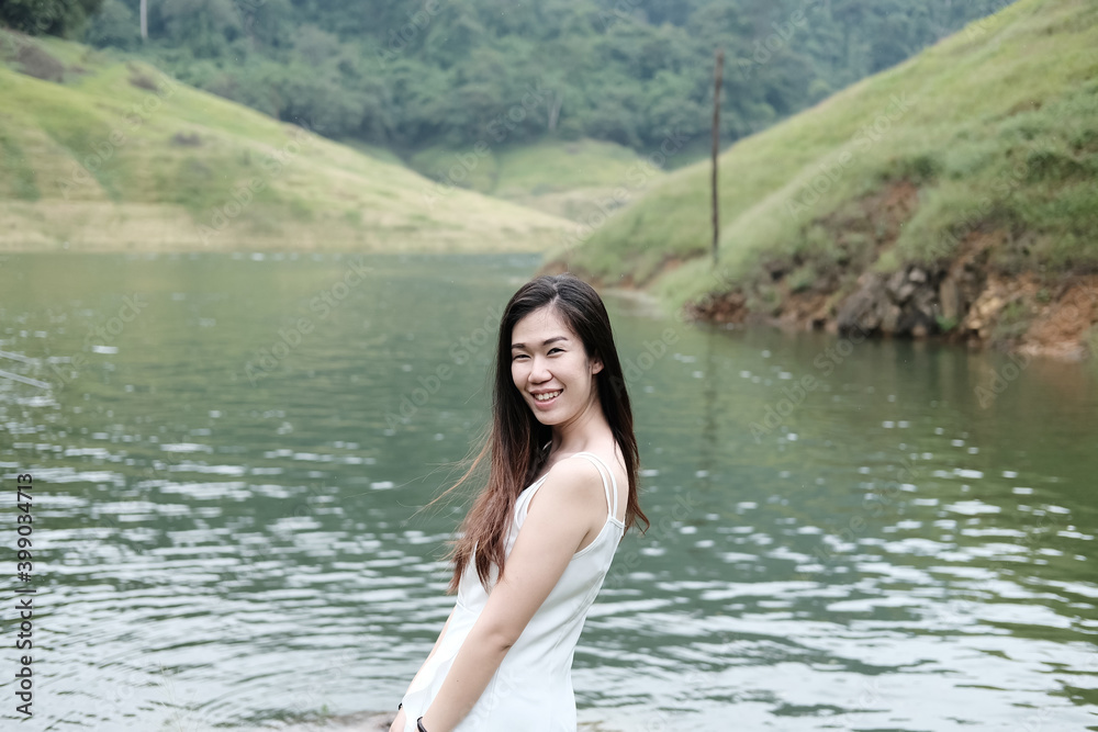 Fototapeta premium Asian woman wear white dress is smiling near the river in forest. Freedom life in nature Concept.
