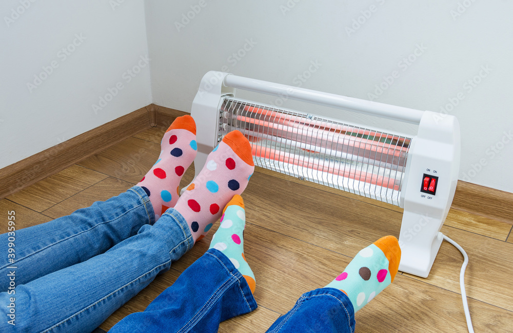 Φωτογραφία A young family wearing bright polka dot socks warms their cold feet near an electric heater